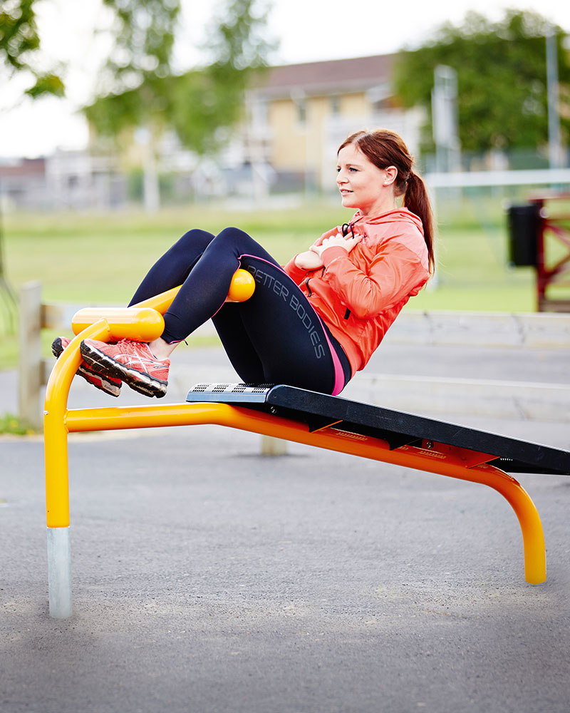 A woman completes sit ups at an outdoor gym bench.